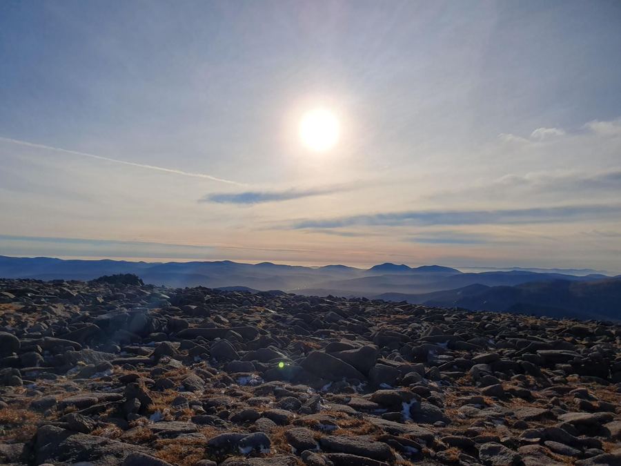The boulder-strewn summit plateau of Ben Macdui at sunset, low sun over distant hills.