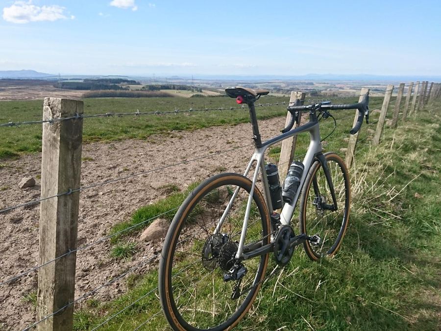 A road bike leaning against a fence post on open moorland under a bright sky.